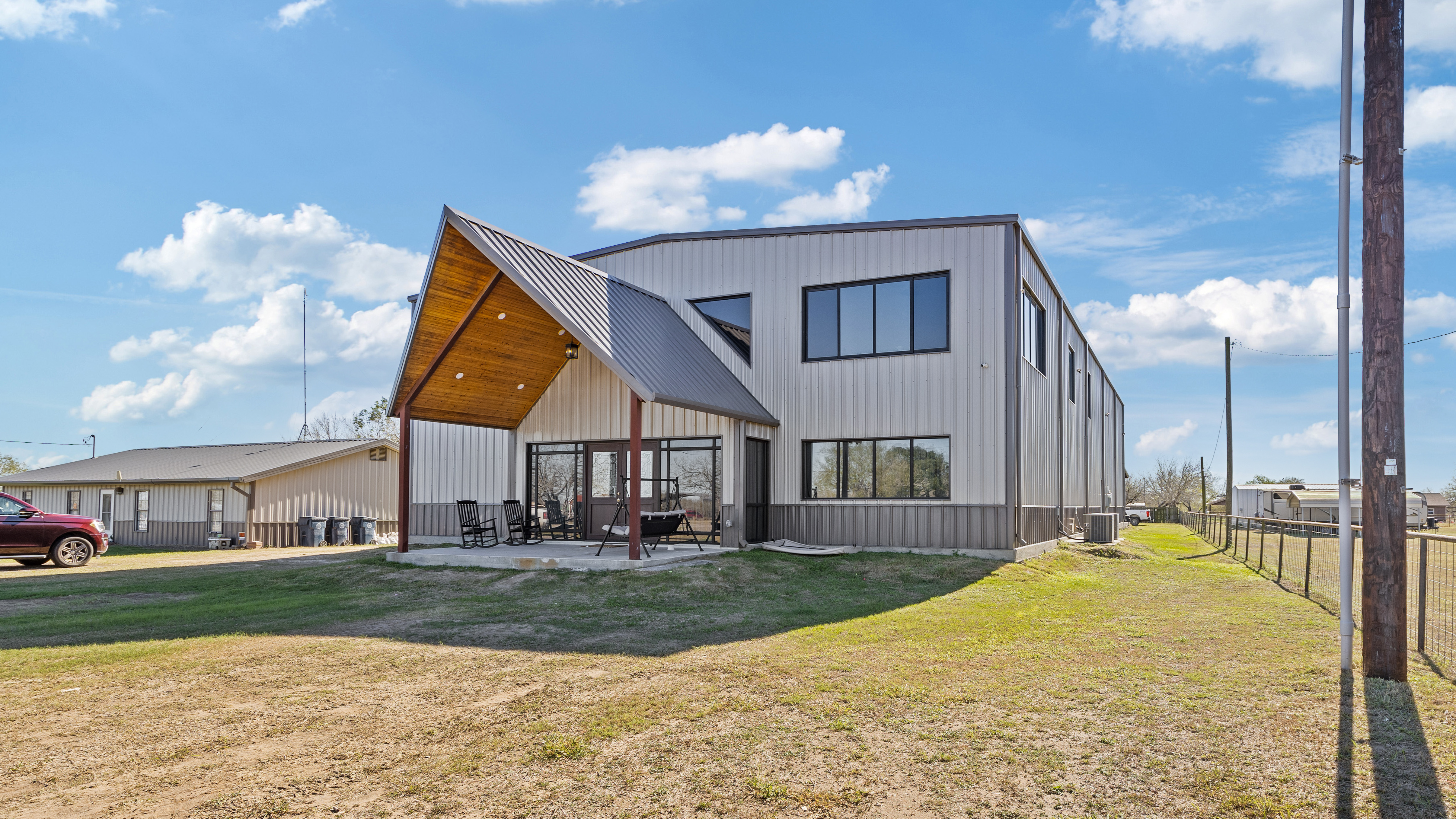 Barndominium-style custom home exterior with metal siding, covered front porch, black-framed windows, and wood ceiling detail.