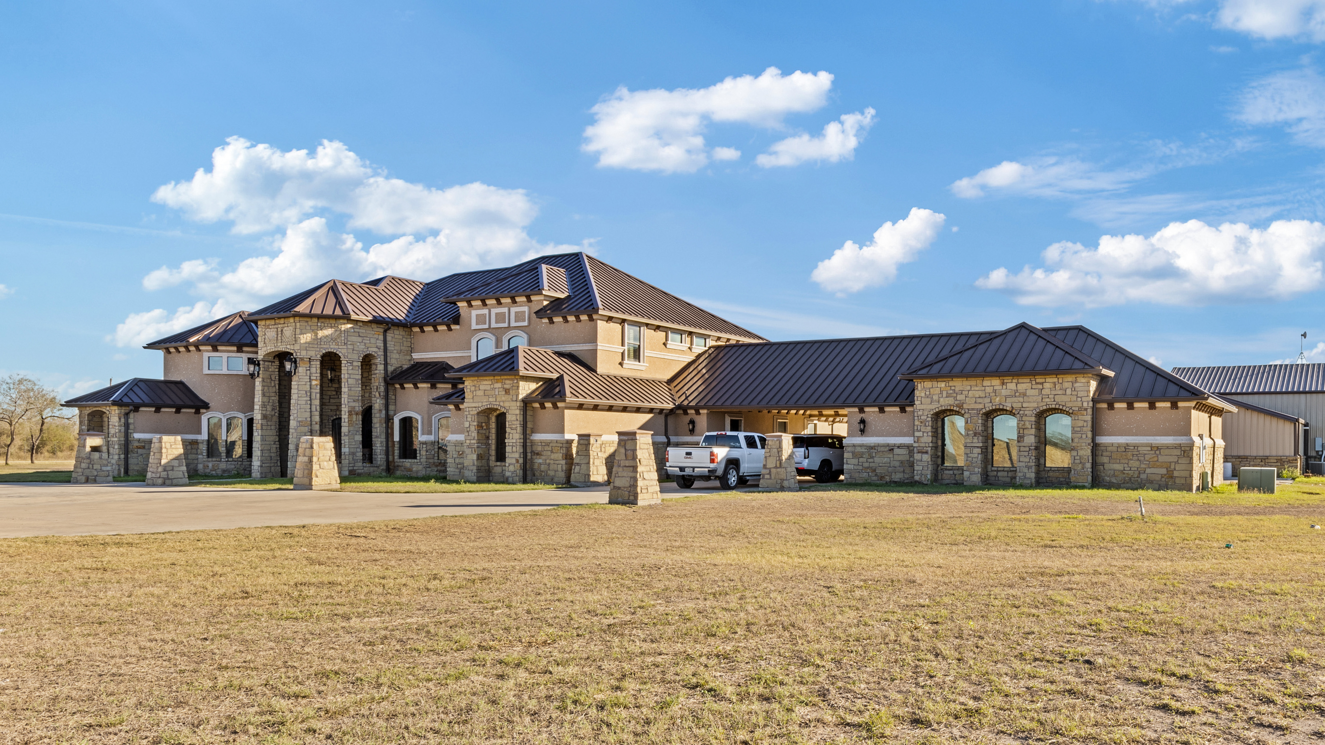 Brick modern farmhouse exterior with black metal roof, large windows, and covered front entry by South Texas Builders.