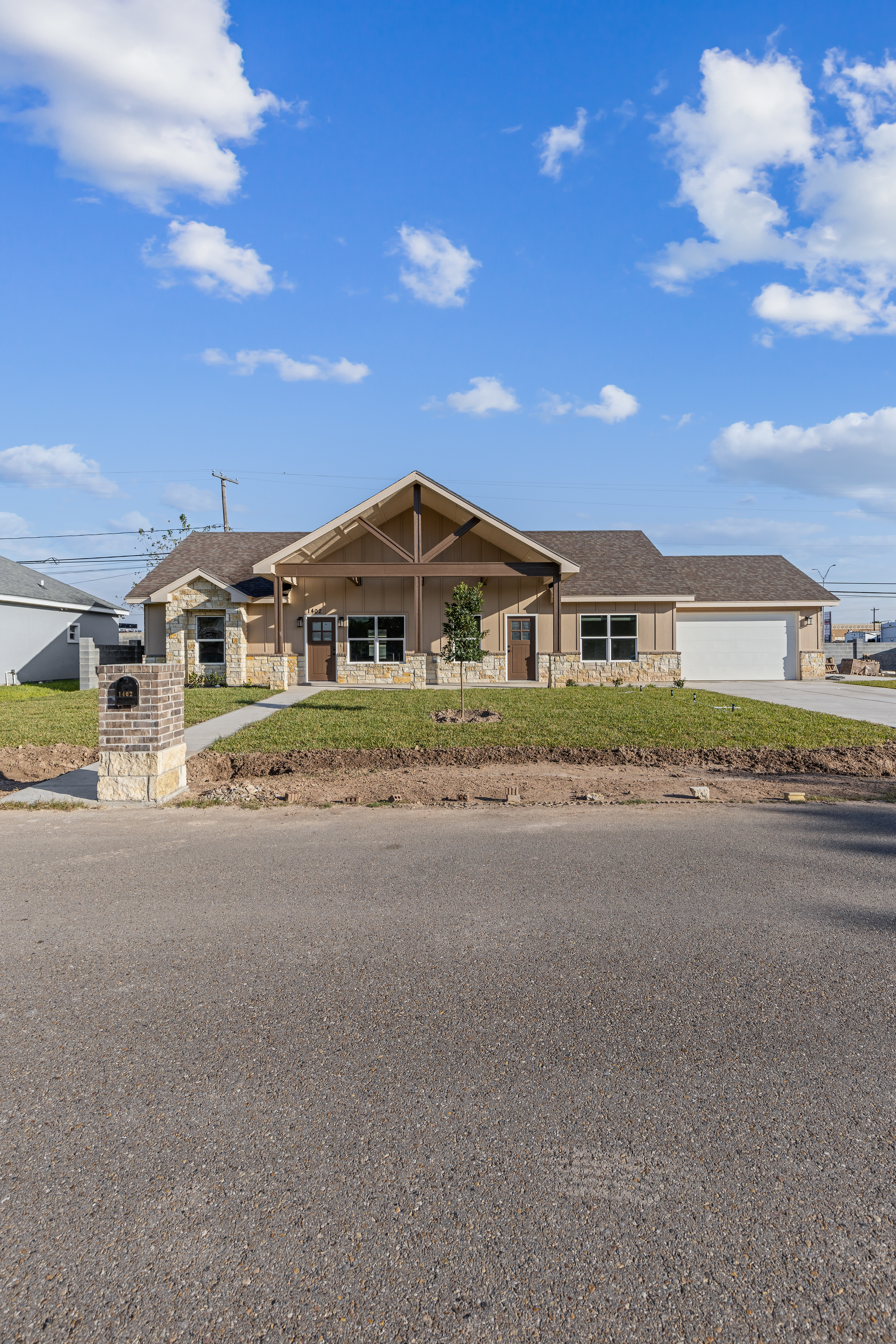 Farmhouse-inspired custom home exterior with stone accents, warm siding, front porch, and two-car garage in South Texas.