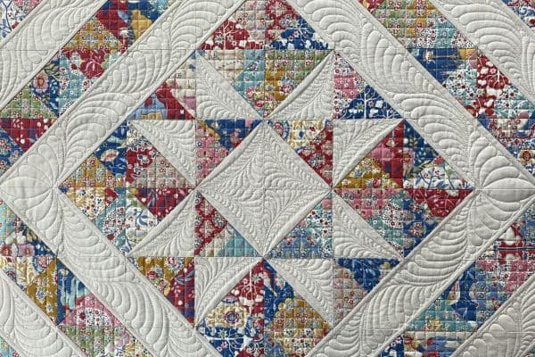 Nærbilde av quilt, lys stjerne på mønstrete bakgrunn. Tett og intrikat quilting i stjernen i kontrast til et enkelt rutenett over den mønstrede bakgrunnen.