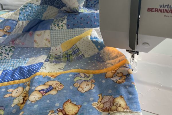 Halvferdig babyquilt i blåtoner under en vanlig symaskin