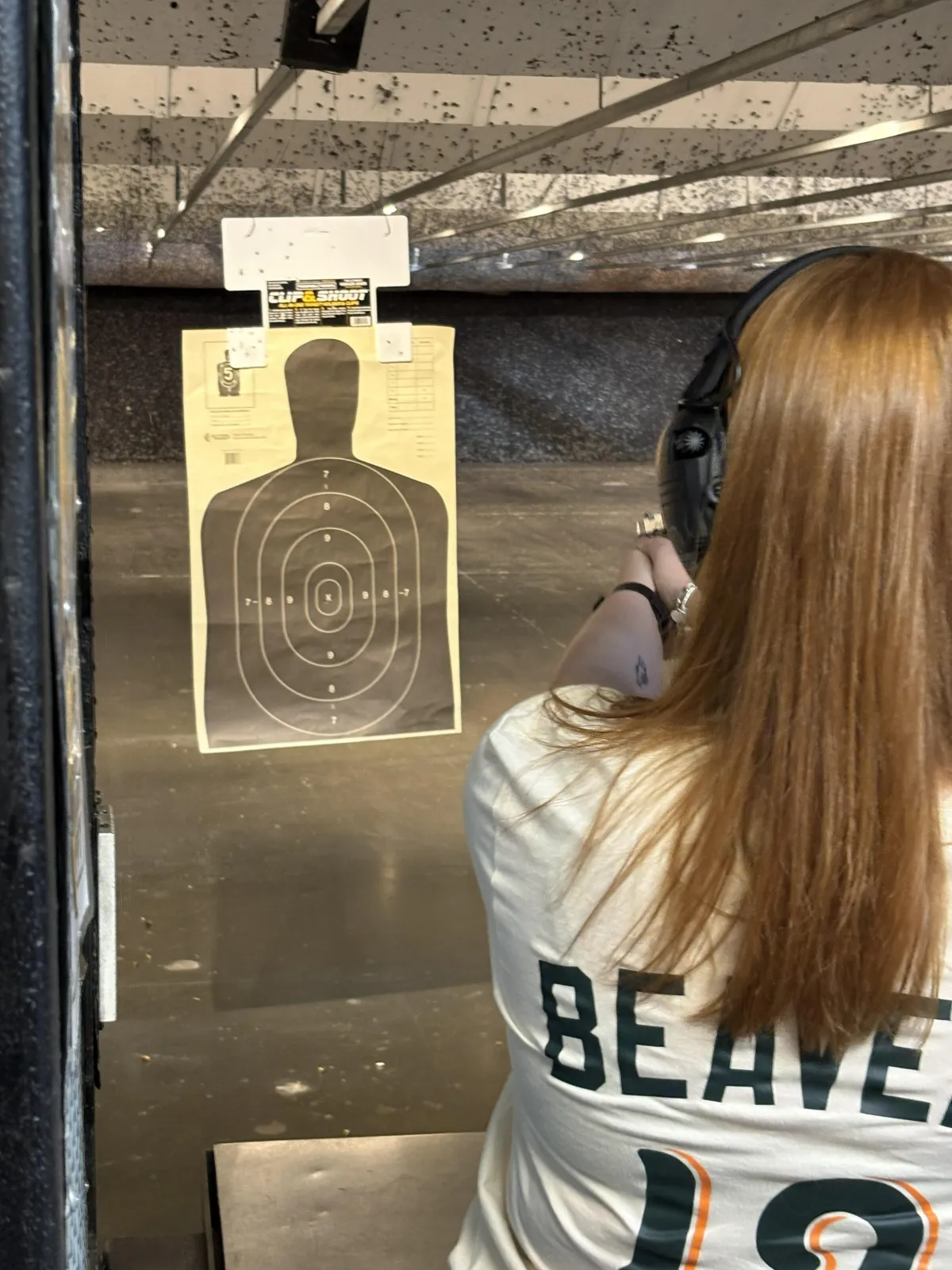 Beginner student practicing safe handgun stance with hearing protection Instructor guiding a new shooter through firearms safety training Mantis laser-training system used during beginner firearms class