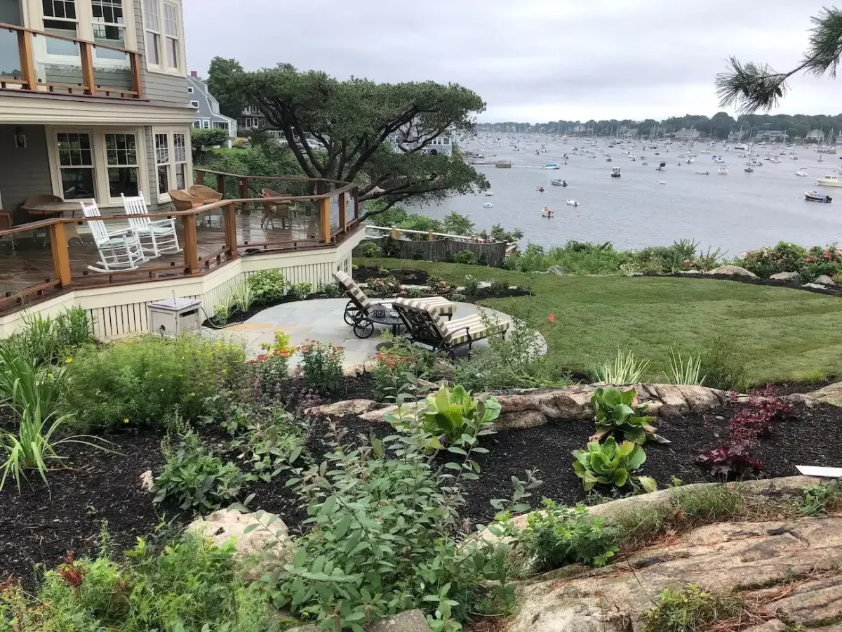 Coastal landscape design in Marblehead MA featuring oceanfront patio, terraced planting beds, and harbor views.