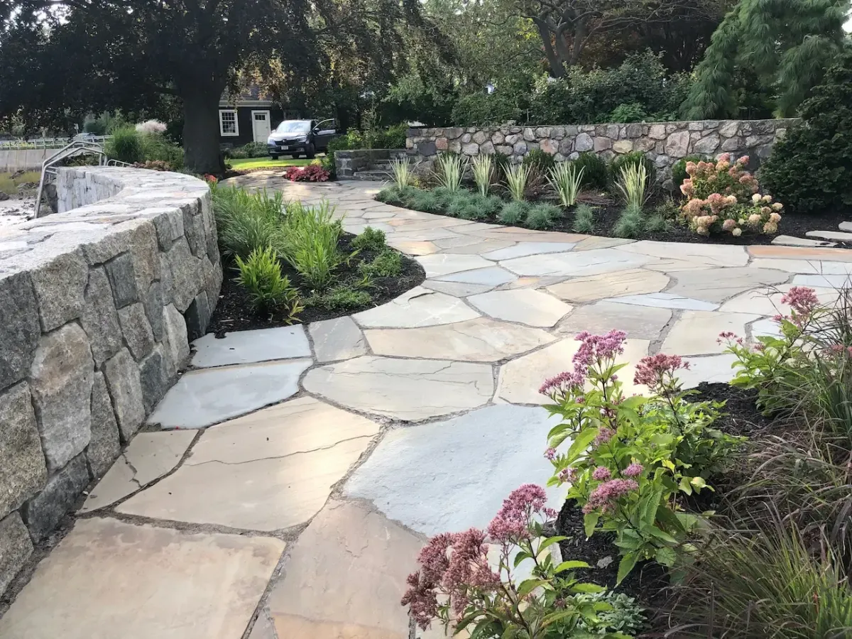 Natural stone patio installation in Marblehead MA with custom planting beds and curved retaining wall.