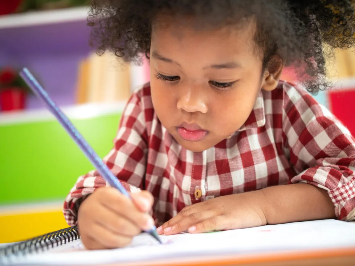 Child writes A in green sand