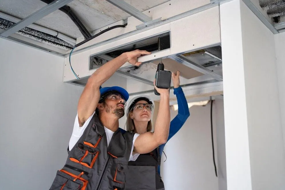 HVAC technicians performing maintenance and repair on a ceiling unit, ensuring efficient operation for energy-saving solutions.
