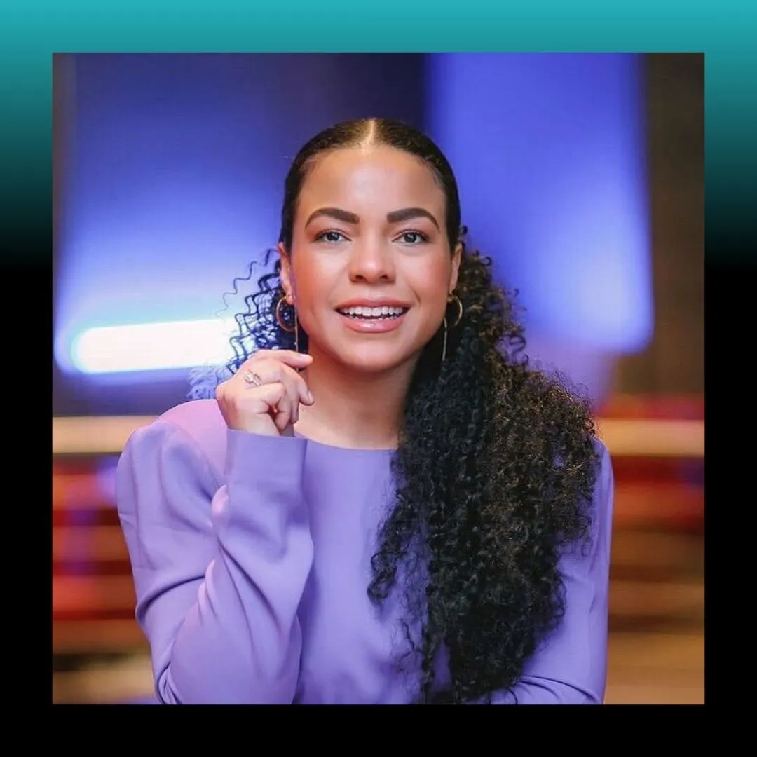 Headshot of a smiling woman in a purple top against a blue background