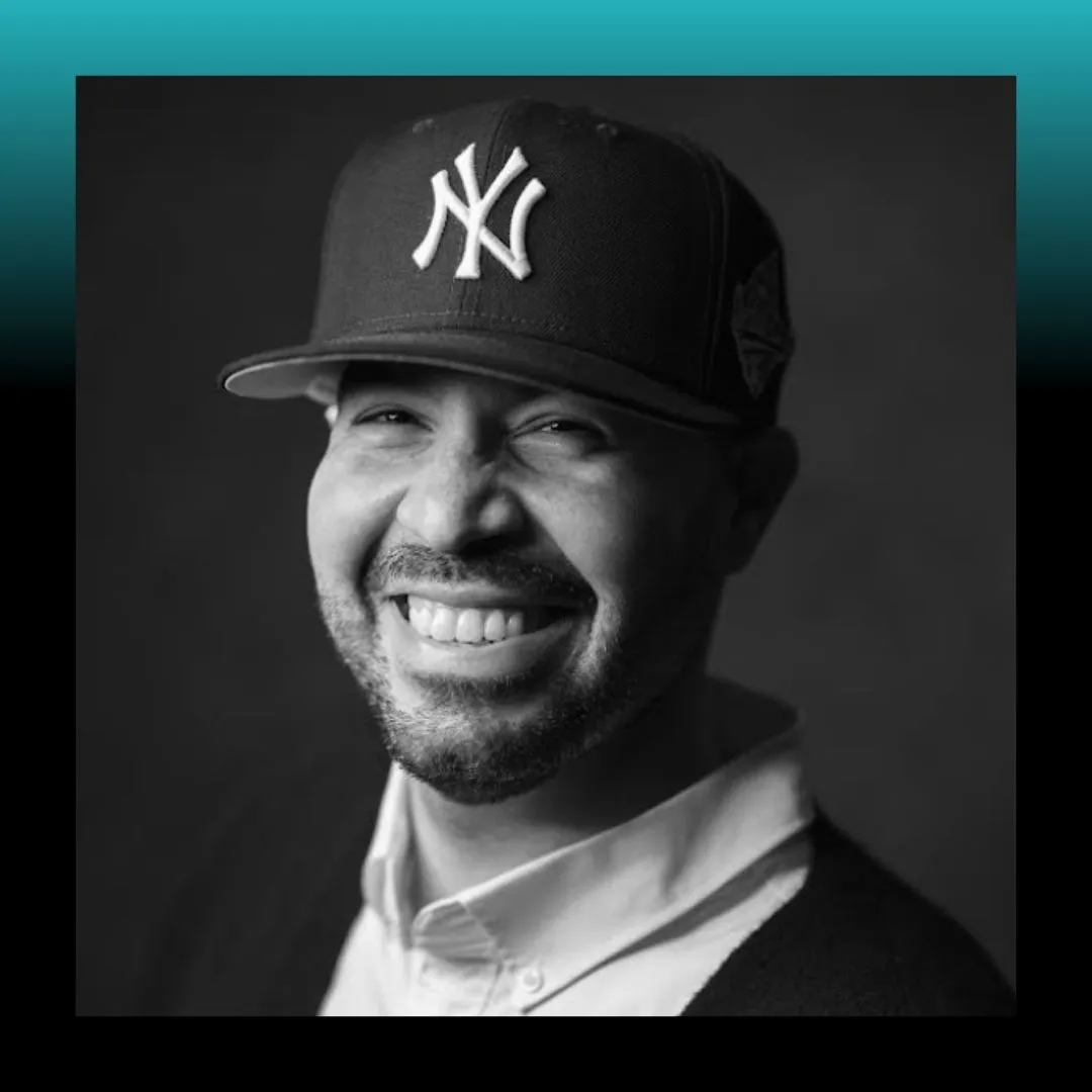 Headshot of a man wearing a baseball cap against a blue background