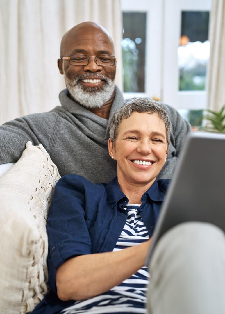 Retired mixed-race couple smiling and looking at laptop