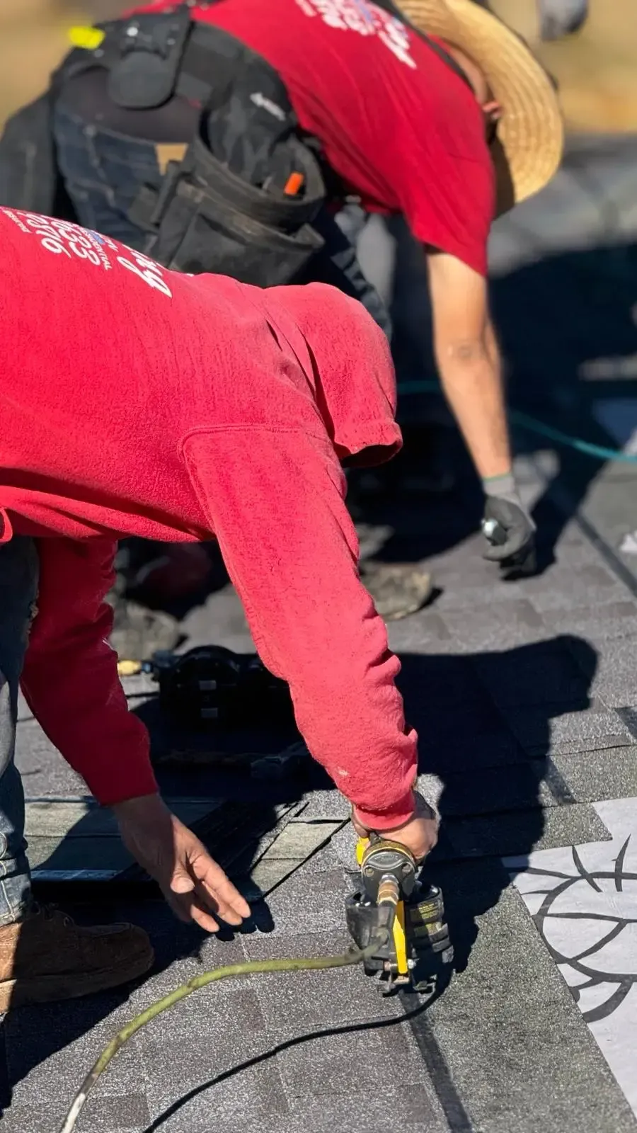 Roofer nailing shingles on dark asphalt roof during repair — roof repair near me Riverside County