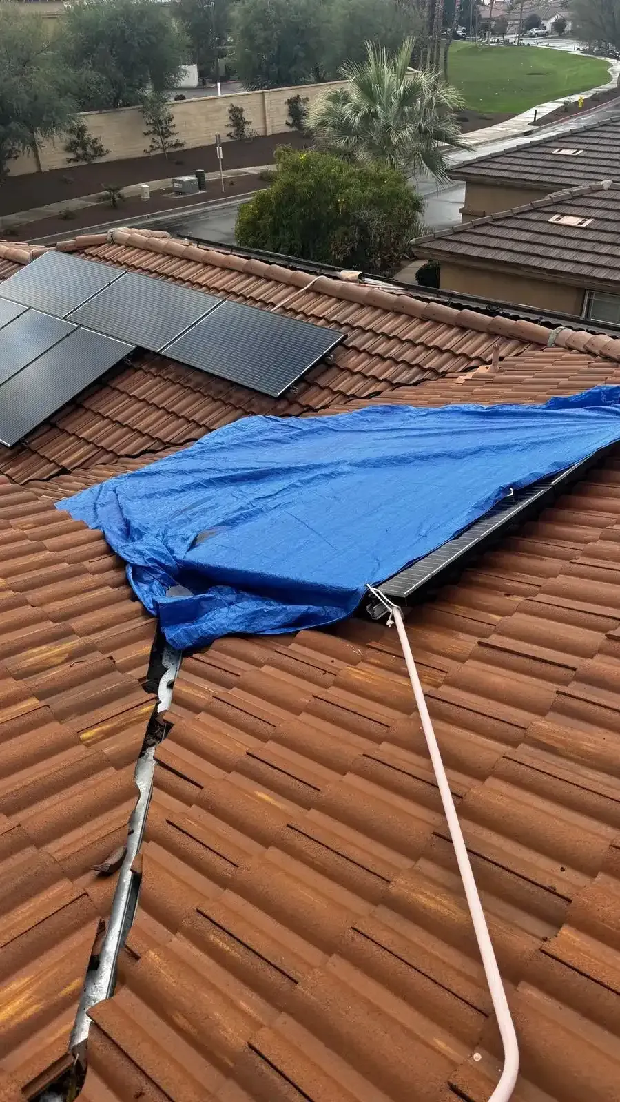 Emergency blue tarp covering storm damaged tile roof  section with solar panels on Southern California home