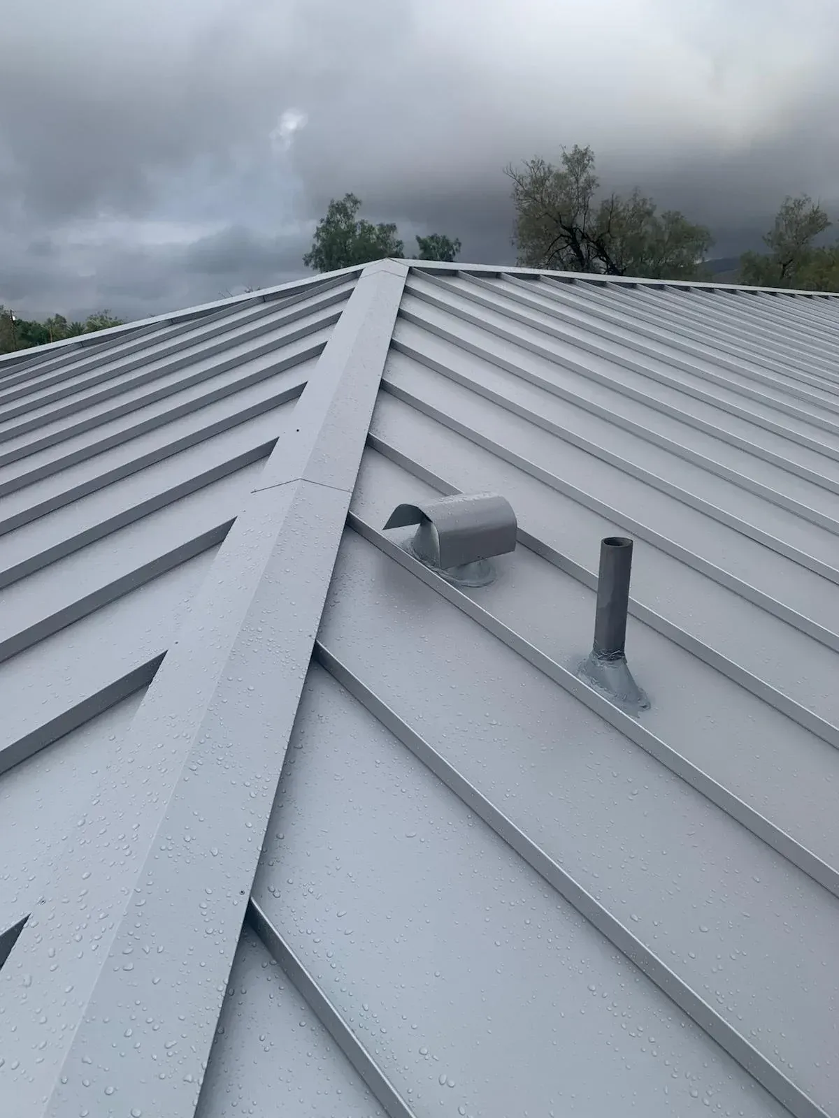 Close up of standing seam metal roof ridge detail  with flashed vent penetration by Dove Roofing Southern California