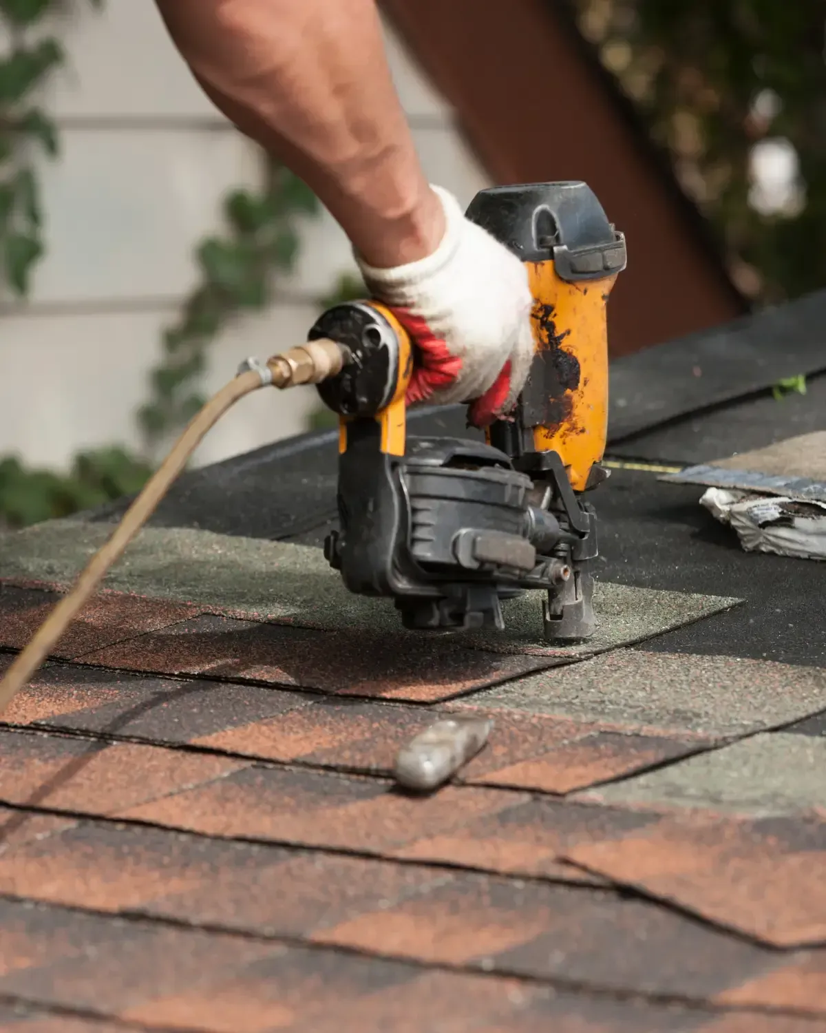 Close-up of pneumatic nail gun fastening new asphalt shingles — how do you install roof shingles