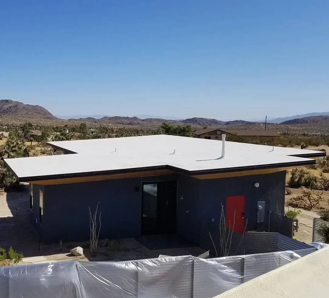 White flat roof on modern dark desert home with mountain backdrop — roofing Joshua Tree CA