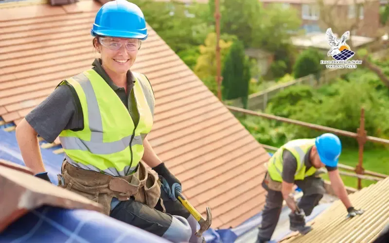 Two roofers in high-visibility vests working on a tile roof surrounded by green trees