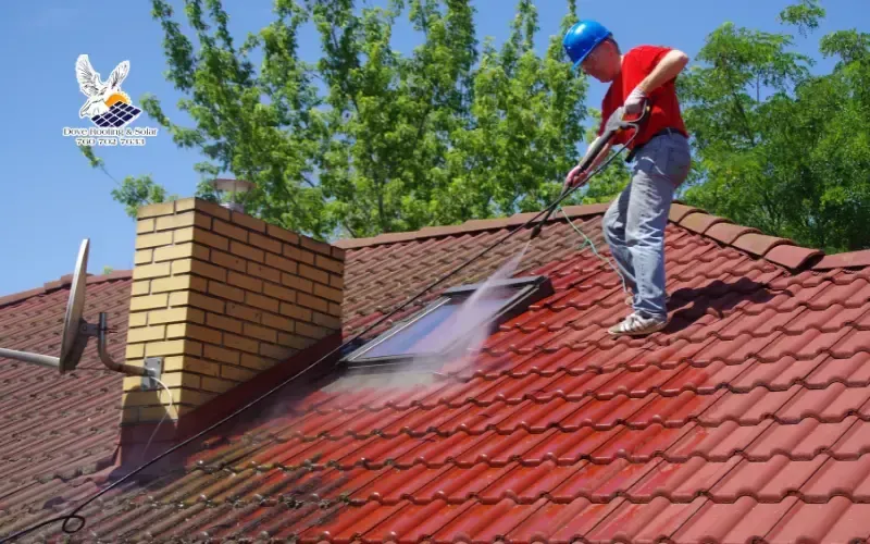 Professional roof washing removing dirt and algae from a tile roof near a chimney