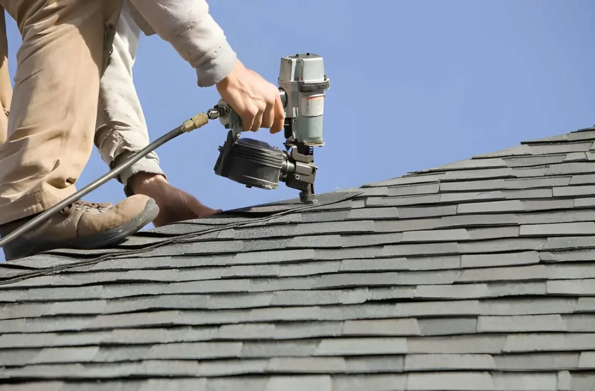 Roofing contractor installing asphalt shingles with a nail gun