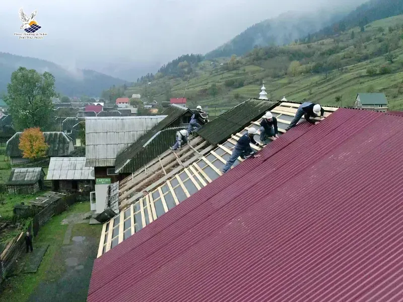 Roofing crew installing metal roofing panels on a rural building.