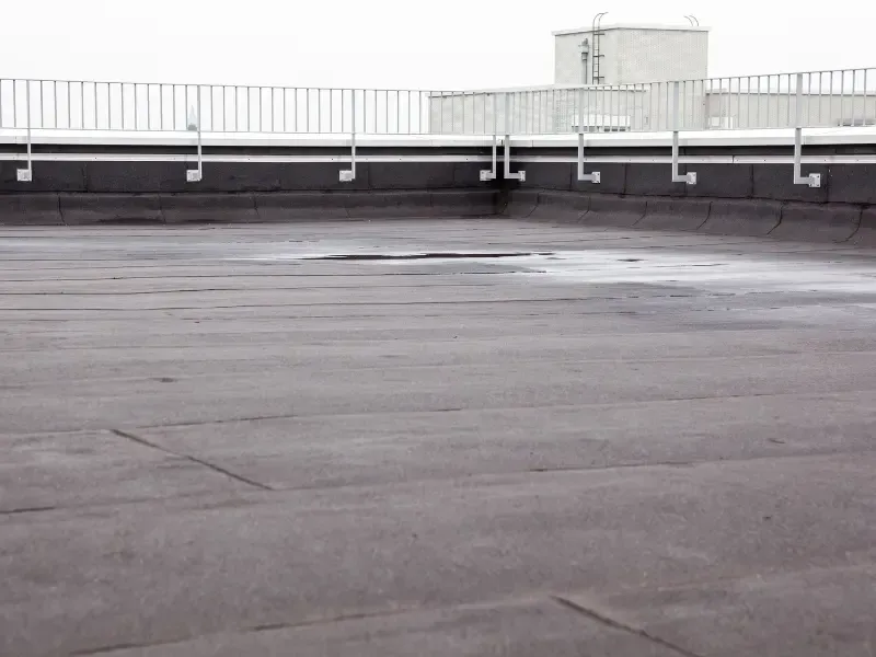 Flat commercial roof with safety railing showing pooling water.