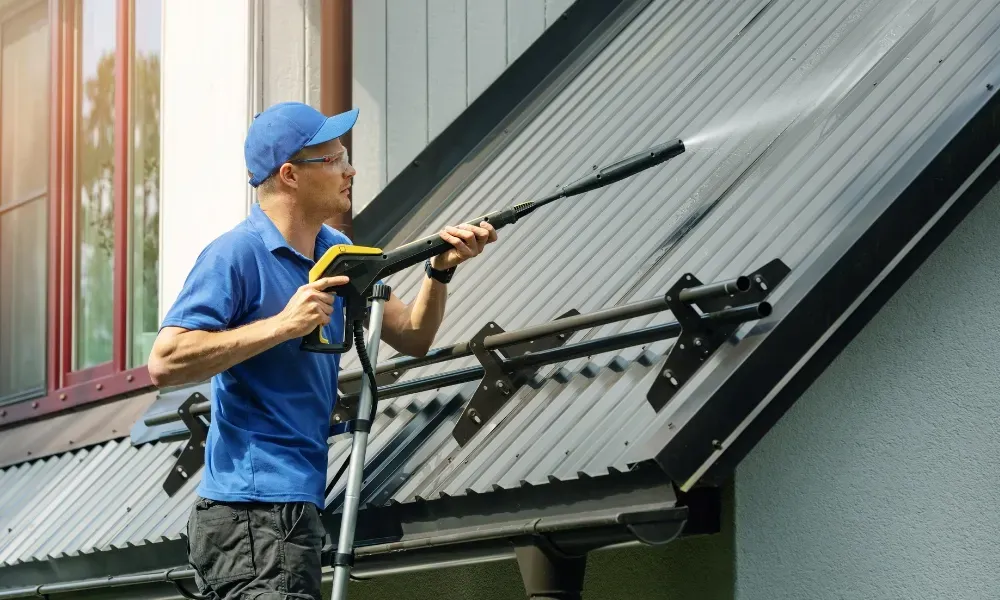 Worker power washing red clay tile roof to remove moss and debris — how to remove moss from roof