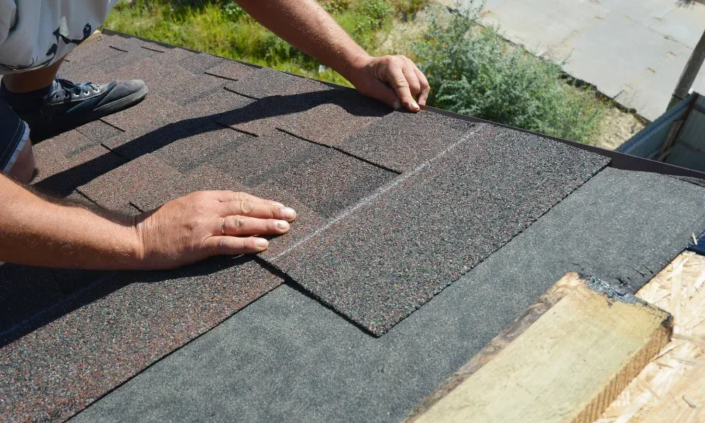 Hand lifting damaged shingle revealing gap at eave — what are signs of roof damage after a storm