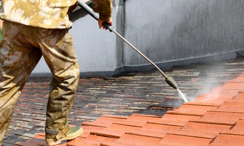 Worker power washing red clay tile roof to remove moss and debris — how to remove moss from roof