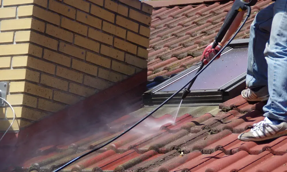 Worker power washing red clay tile roof to remove moss and debris — how to remove moss from roof