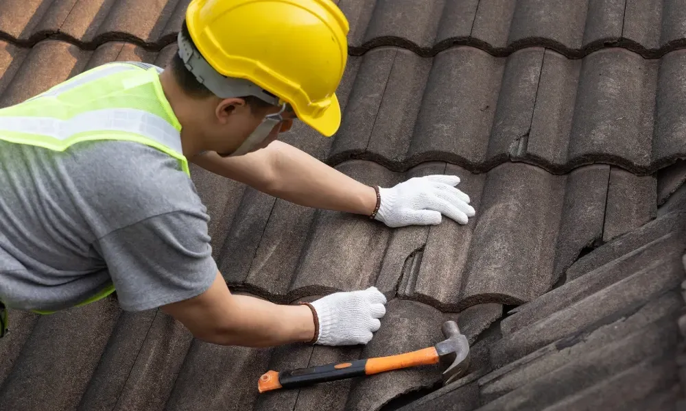 Hand lifting damaged shingle revealing gap at eave — what are signs of roof damage after a storm