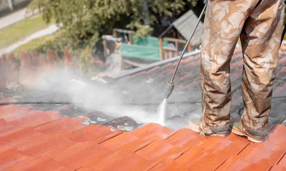 Worker power washing red clay tile roof to remove moss and debris — how to remove moss from roof