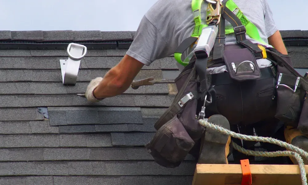 Hand lifting damaged shingle revealing gap at eave — what are signs of roof damage after a storm