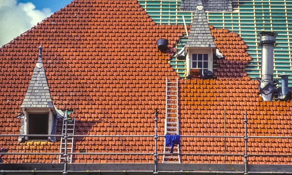 Gloved hand operating nail gun fastening brown asphalt shingles — how do you install roof shingles