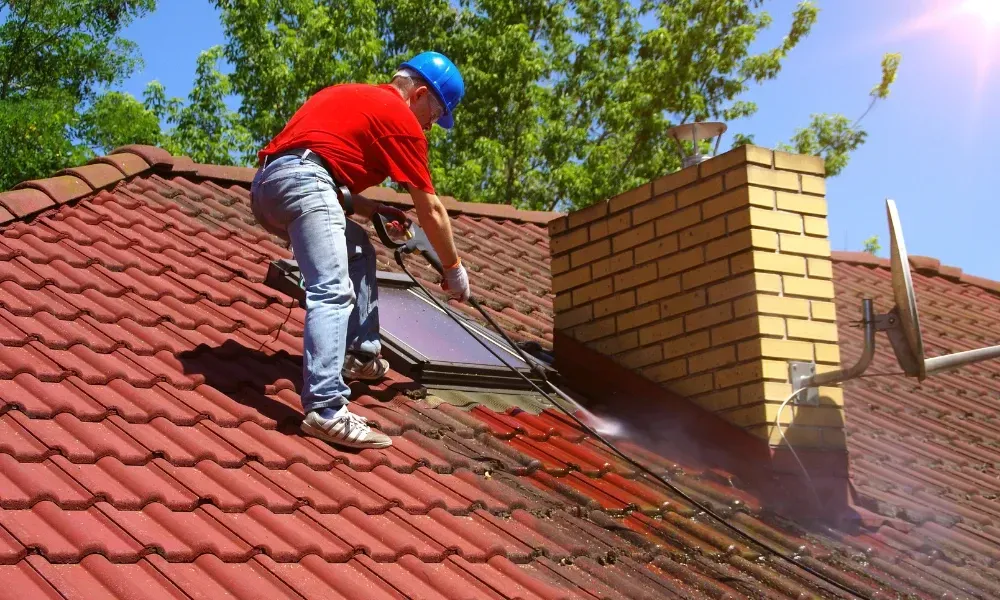 Worker power washing red clay tile roof to remove moss and debris — how to remove moss from roof