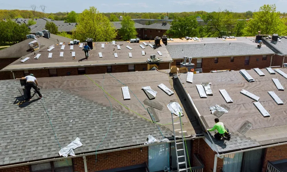 Gloved hand operating nail gun fastening brown asphalt shingles — how do you install roof shingles