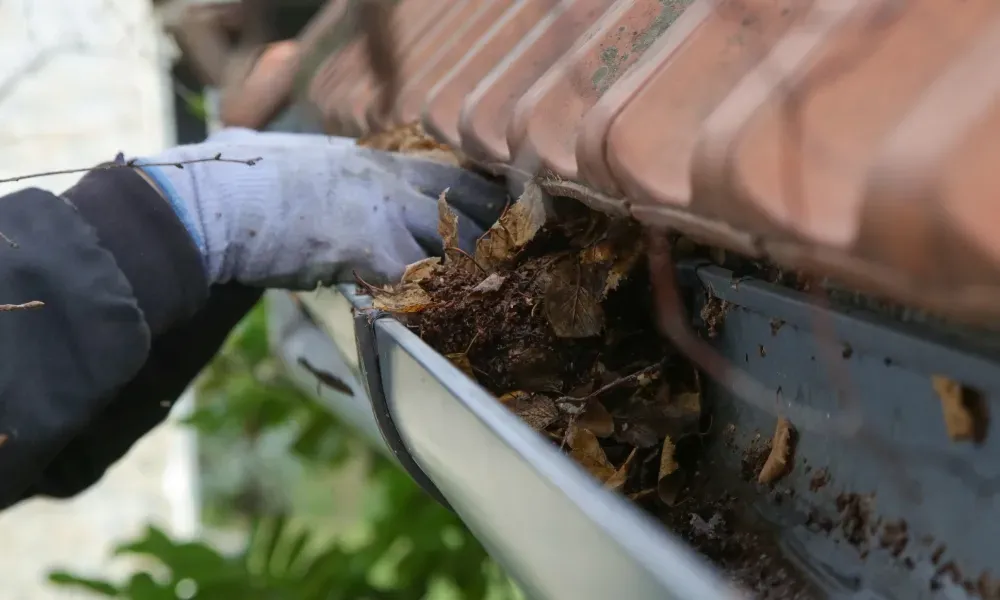 Worker power washing red clay tile roof to remove moss and debris — how to remove moss from roof