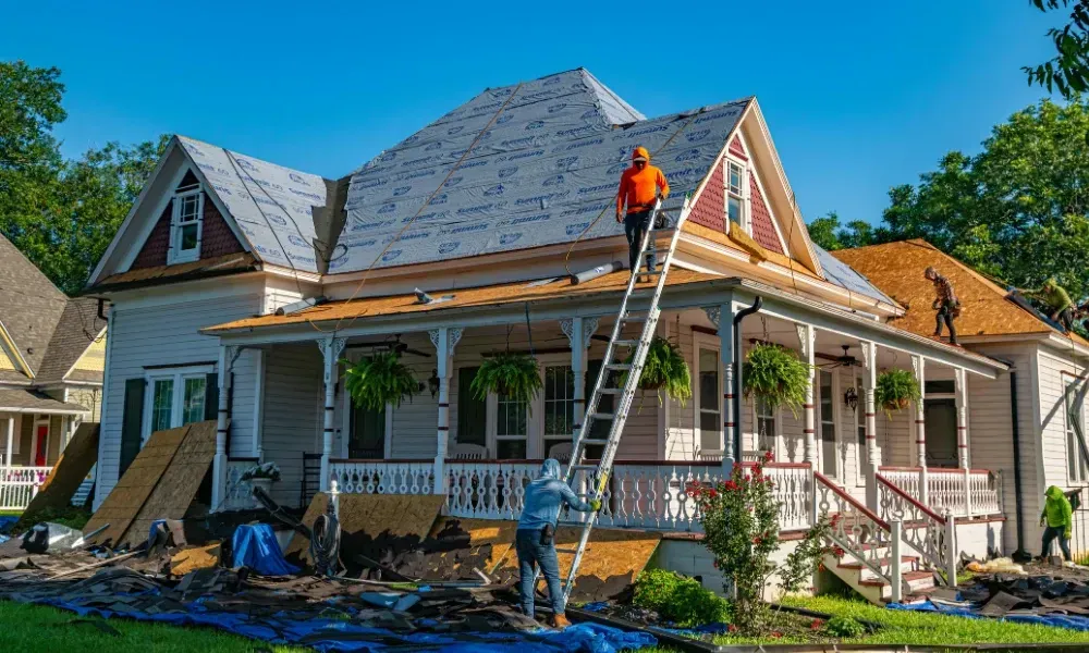 Gloved hand operating nail gun fastening brown asphalt shingles — how do you install roof shingles