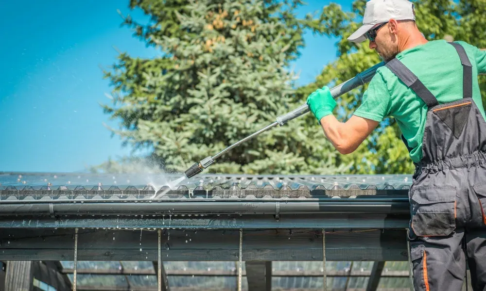 Worker power washing red clay tile roof to remove moss and debris — how to remove moss from roof