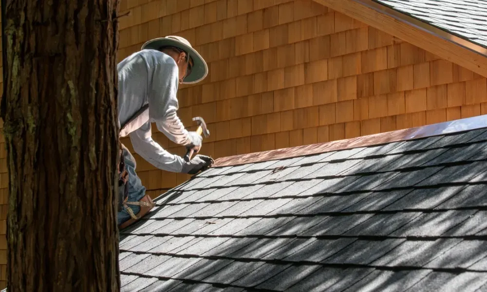 Gloved hand operating nail gun fastening brown asphalt shingles — how do you install roof shingles