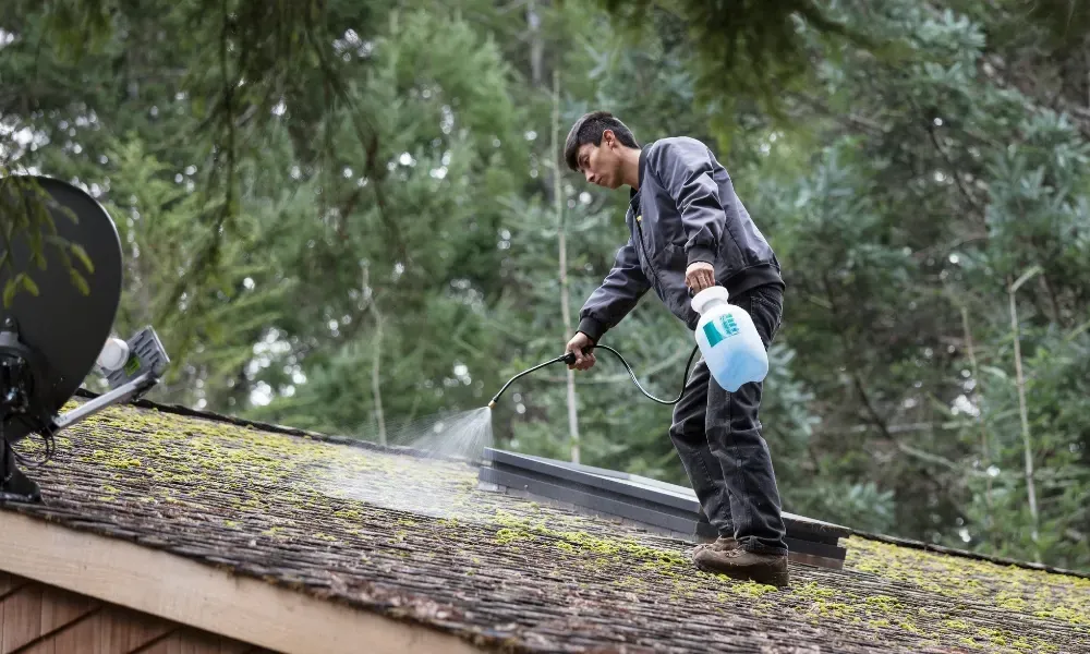 Worker power washing red clay tile roof to remove moss and debris — how to remove moss from roof