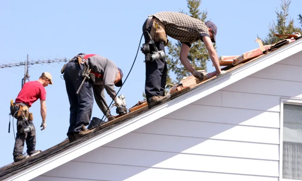 Gloved hand operating nail gun fastening brown asphalt shingles — how do you install roof shingles