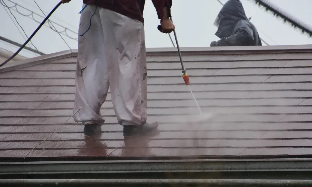 Worker power washing red clay tile roof to remove moss and debris — how to remove moss from roof
