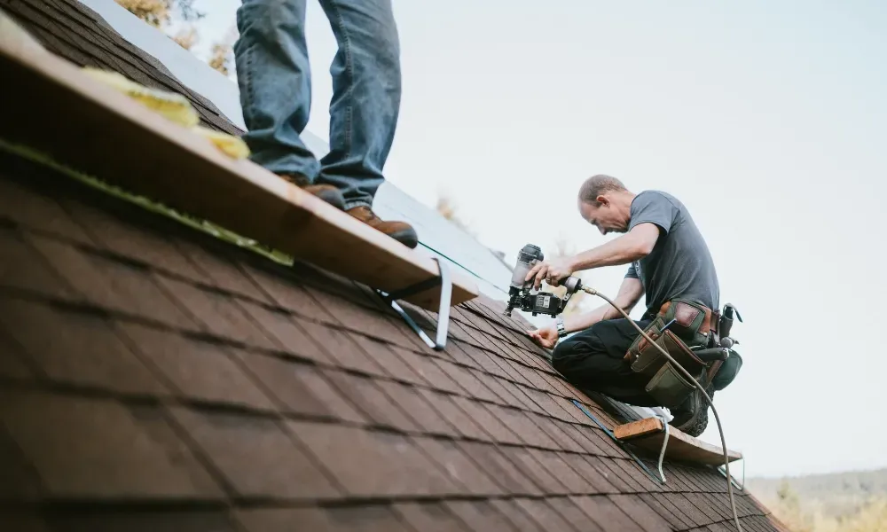 Gloved hand operating nail gun fastening brown asphalt shingles — how do you install roof shingles