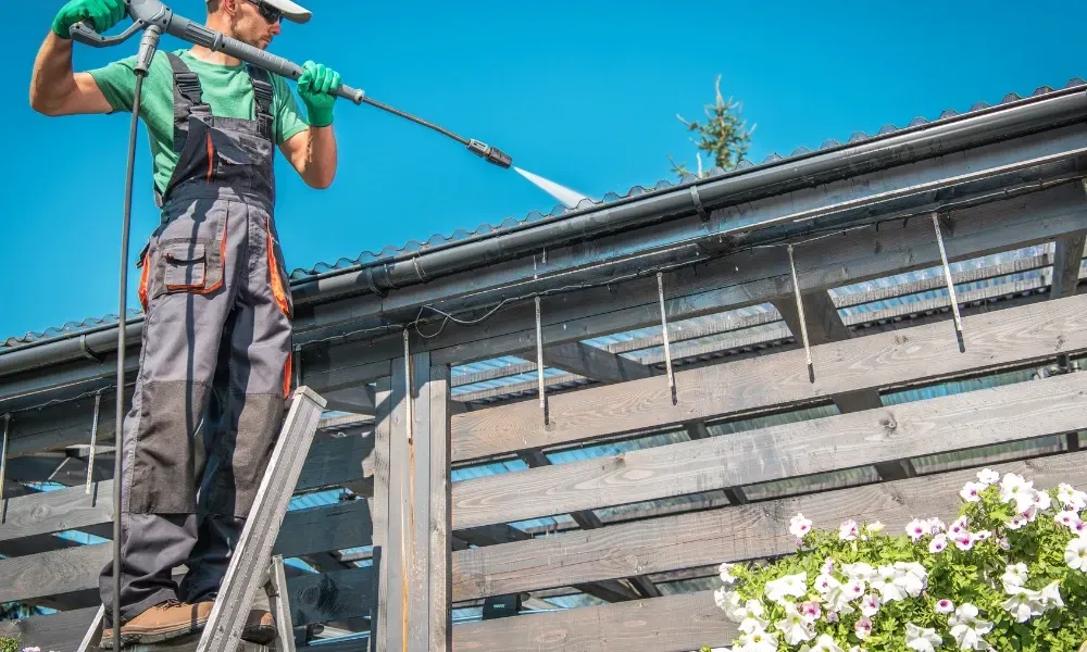 Worker power washing red clay tile roof to remove moss and debris — how to remove moss from roof