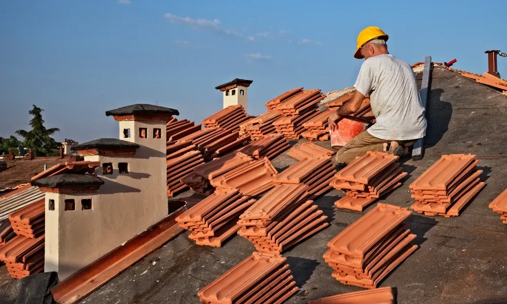 Gloved hand operating nail gun fastening brown asphalt shingles — how do you install roof shingles