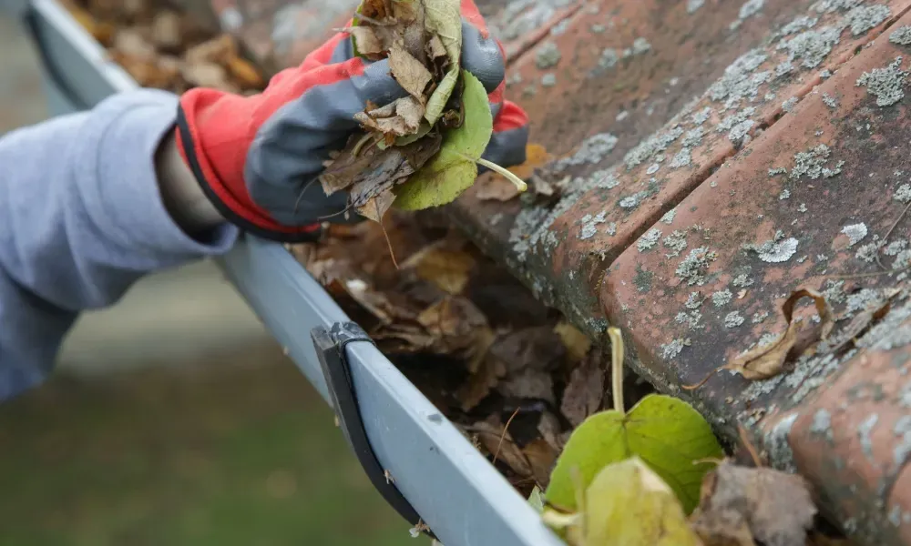 Worker power washing red clay tile roof to remove moss and debris — how to remove moss from roof