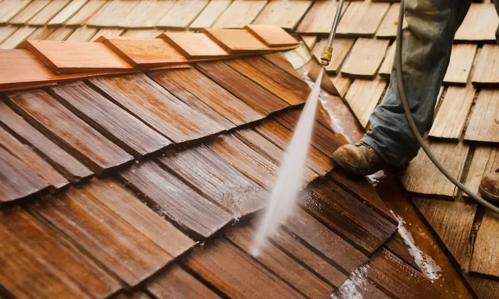 Worker power washing red clay tile roof to remove moss and debris — how to remove moss from roof
