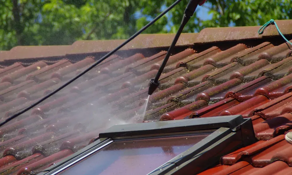 Worker power washing red clay tile roof to remove moss and debris — how to remove moss from roof