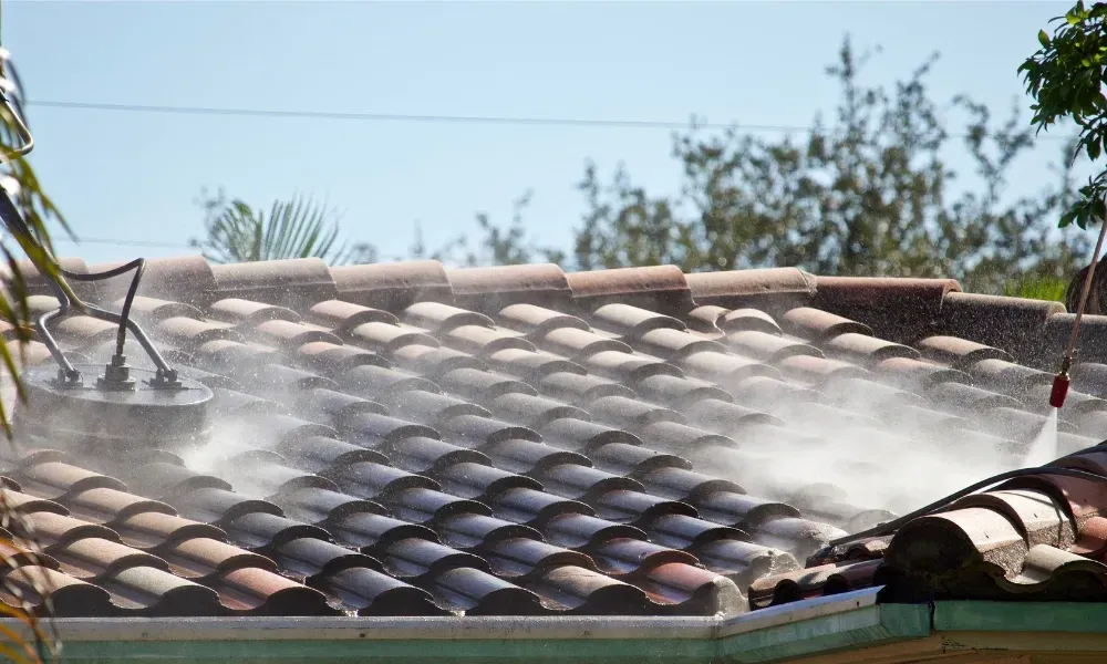 Worker power washing red clay tile roof to remove moss and debris — how to remove moss from roof
