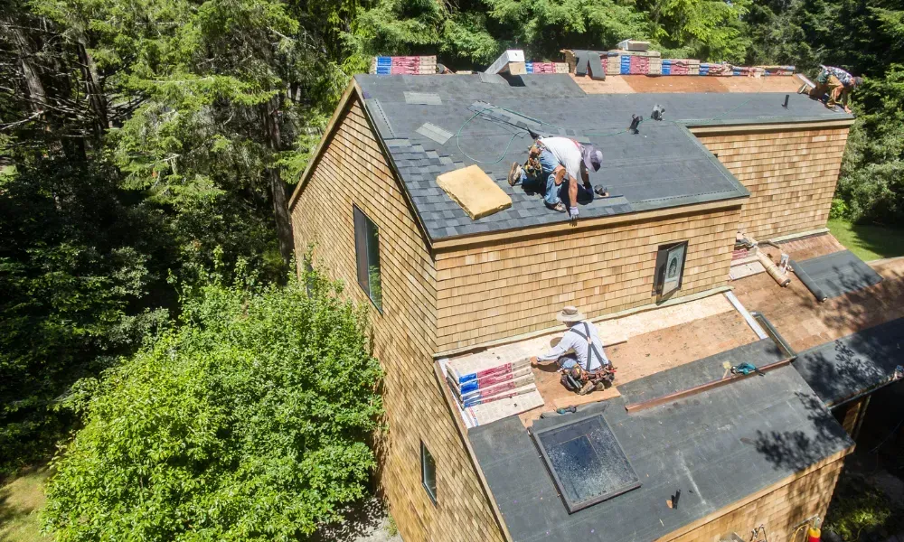 Gloved hand operating nail gun fastening brown asphalt shingles — how do you install roof shingles