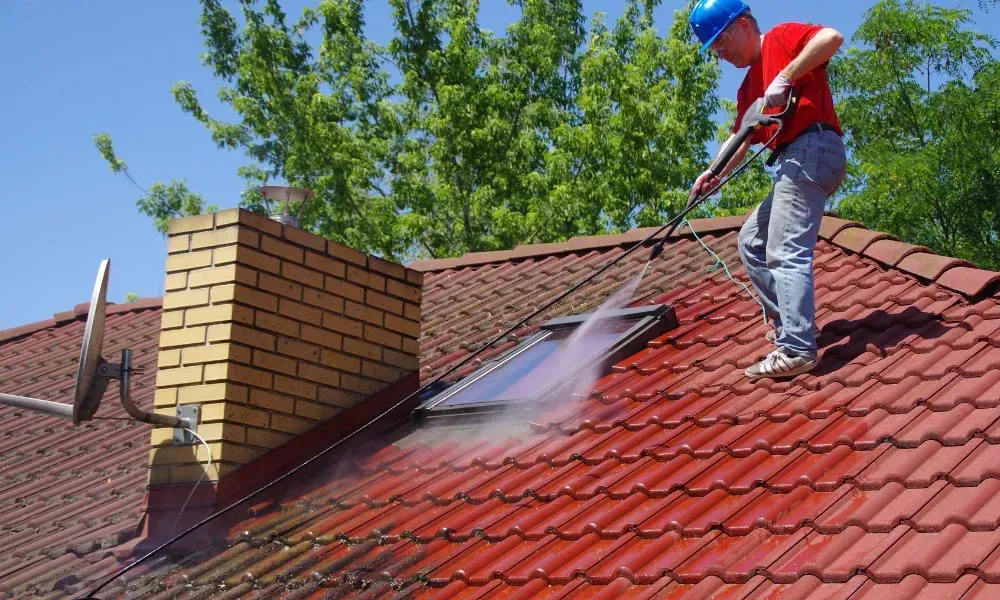 Worker power washing red clay tile roof to remove moss and debris — how to remove moss from roof