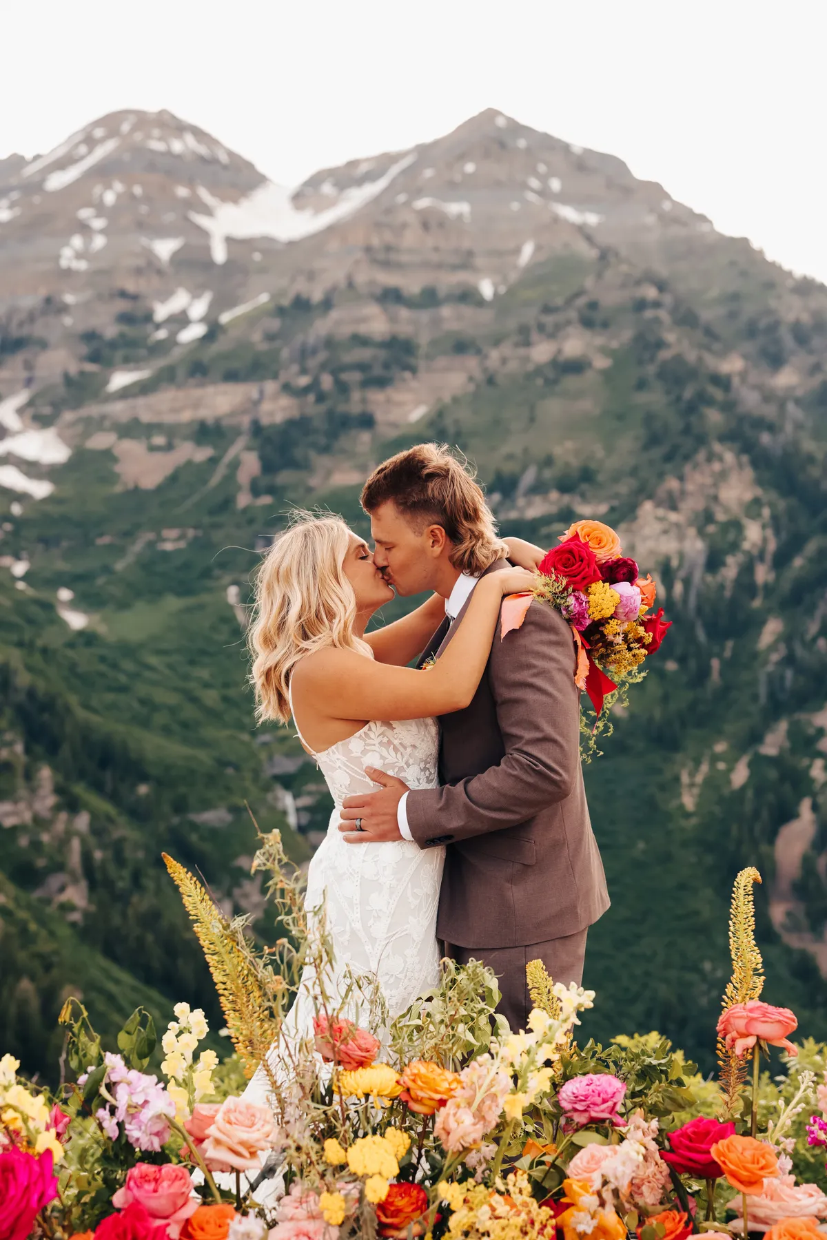 Couple embracing in front of snowcapped peaks and bright florals at Sundance